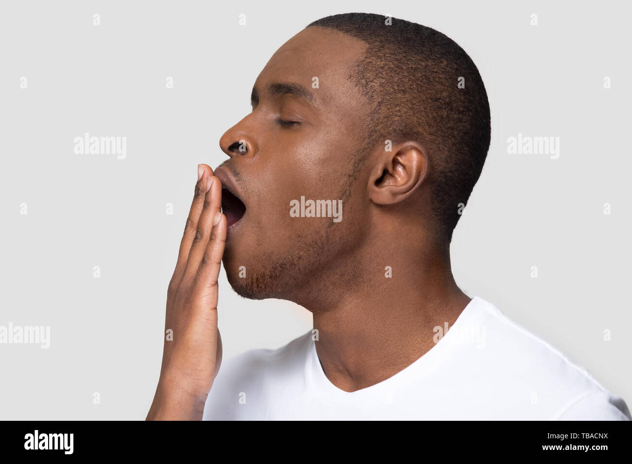 Closeup african male face profile yawning covering mouth with hand Stock Photo