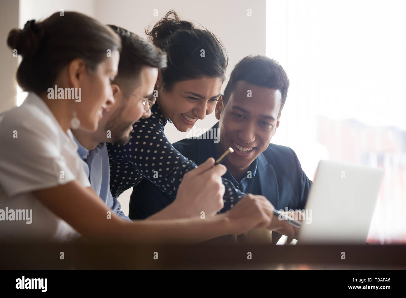 Smiling diverse colleagues laugh brainstorming using laptop Stock Photo