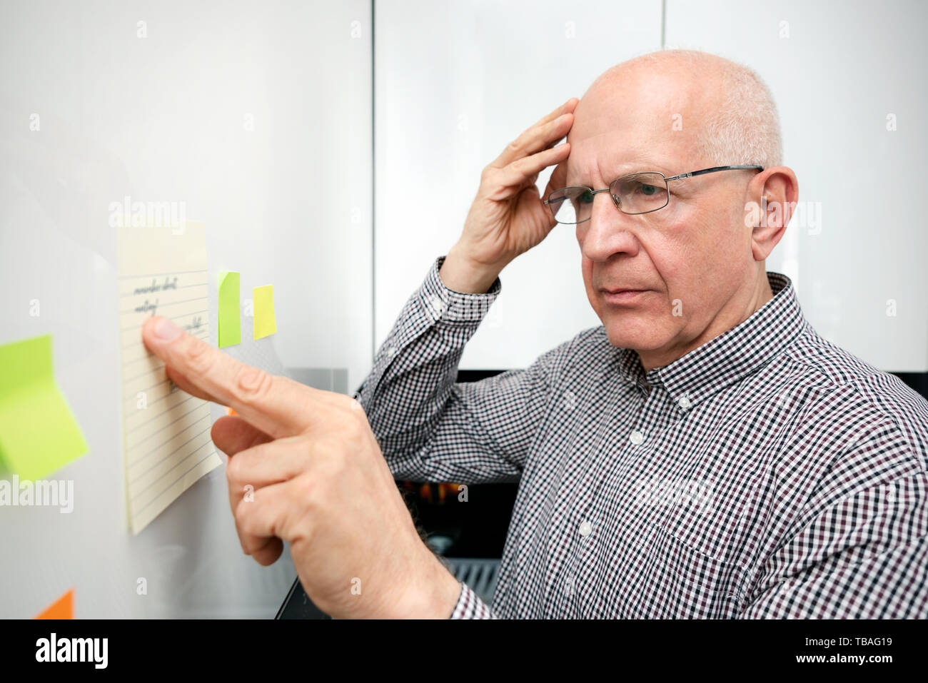 Elderly man looking at notes. Forgetful senior with dementia, memory problem, health concept Stock Photo