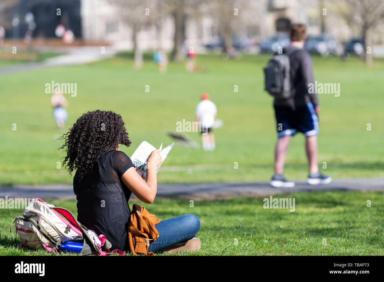 Blacksburg, USA - April 18, 2018: Virginia Tech Polytechnic Institute and State University College campus with student sitting reading book on grass Stock Photo