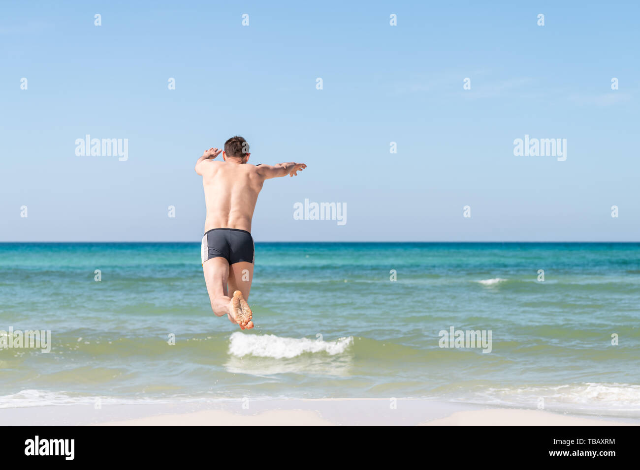 Back of young happy man jumping, diving plunging into ocean water mid-air with arms outstretched in summer in Santa Rosa Beach, Florida Stock Photo