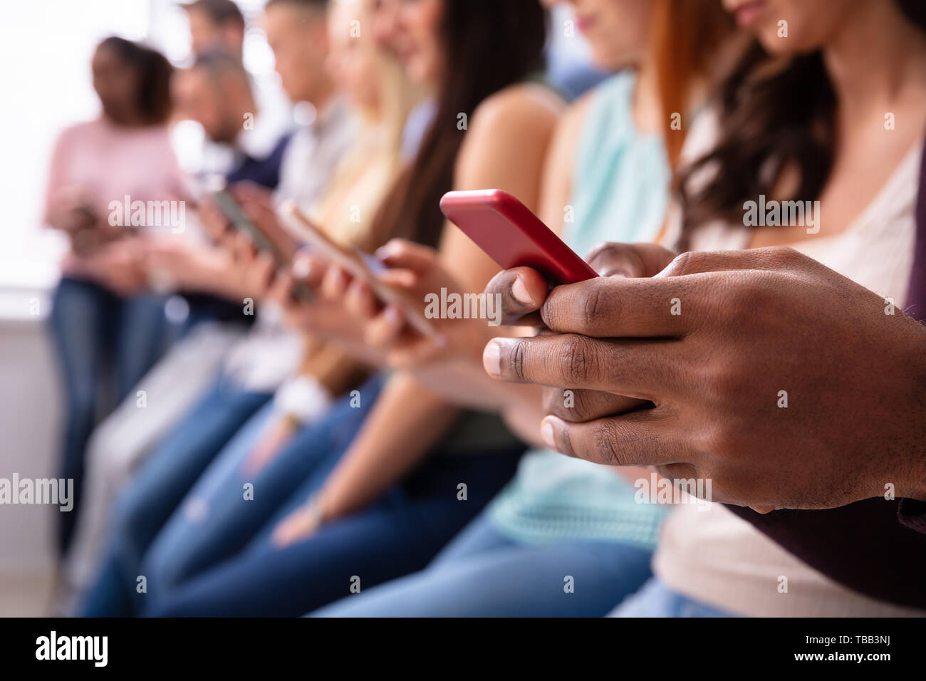 Multi-ethnic Young People Leaning Near Table In Row Using Smartphone Stock Photo