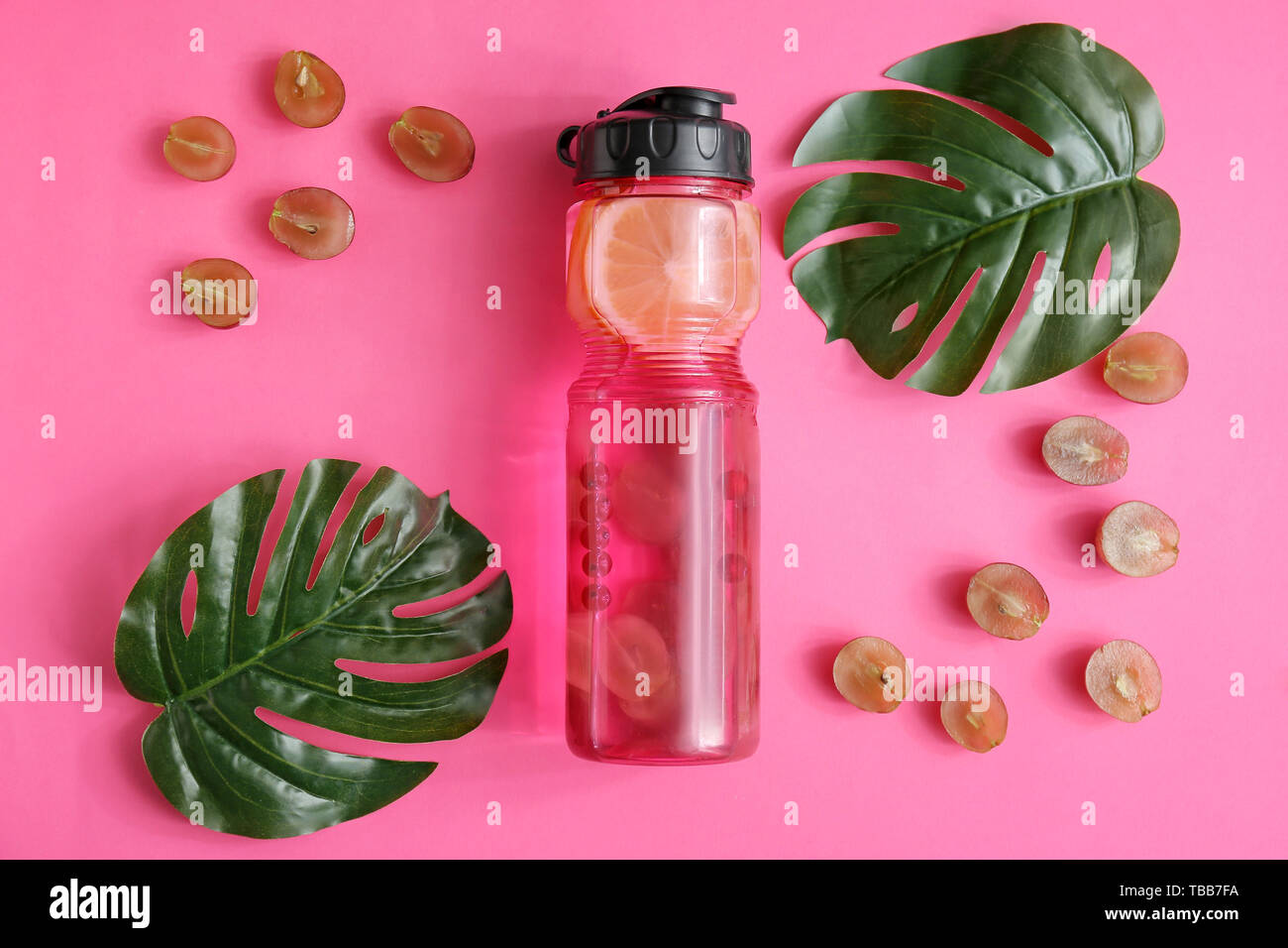 Bottle of infused water, grapes and tropical leaves on color background