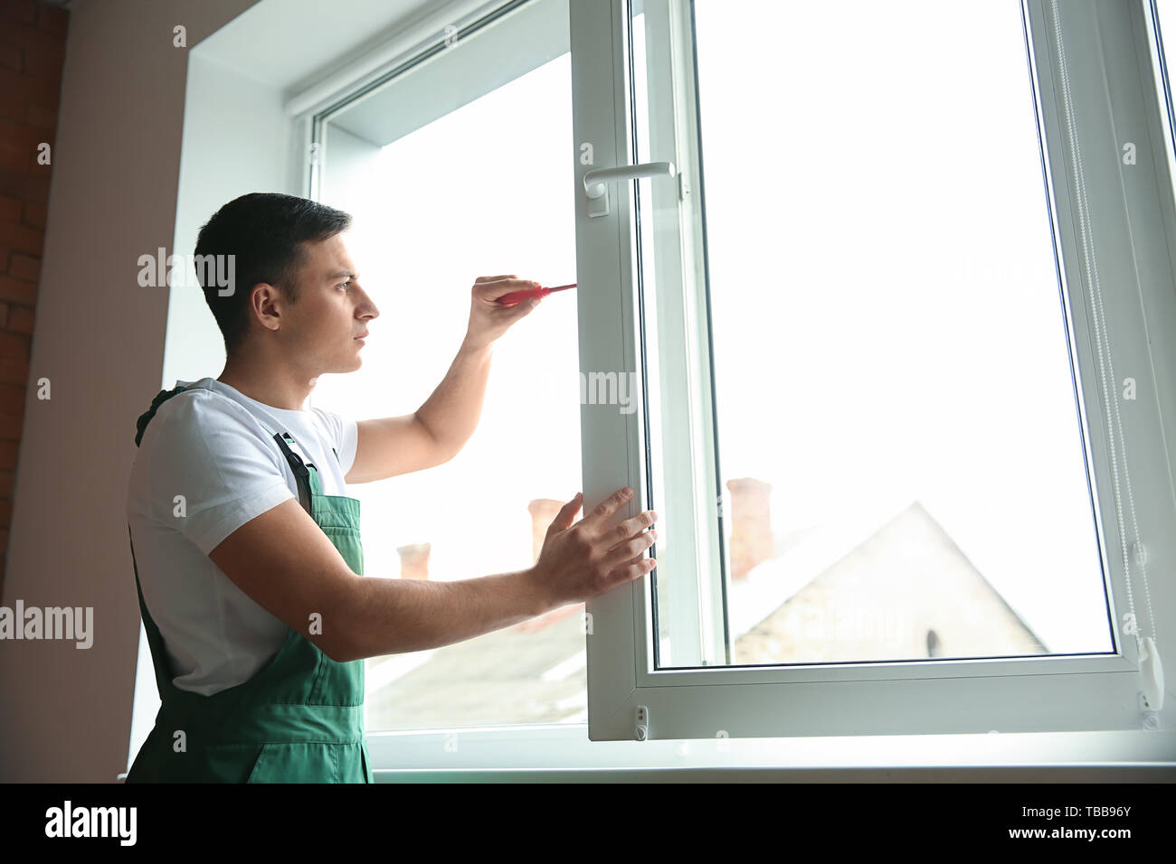 Young worker repairing window in flat Stock Photo