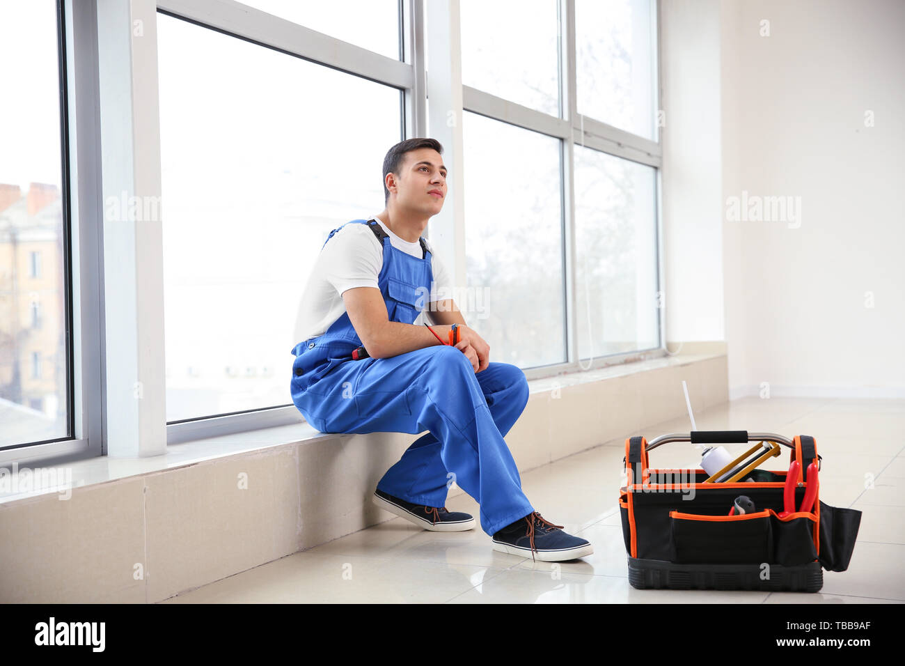Young worker sitting on window sill in flat Stock Photo