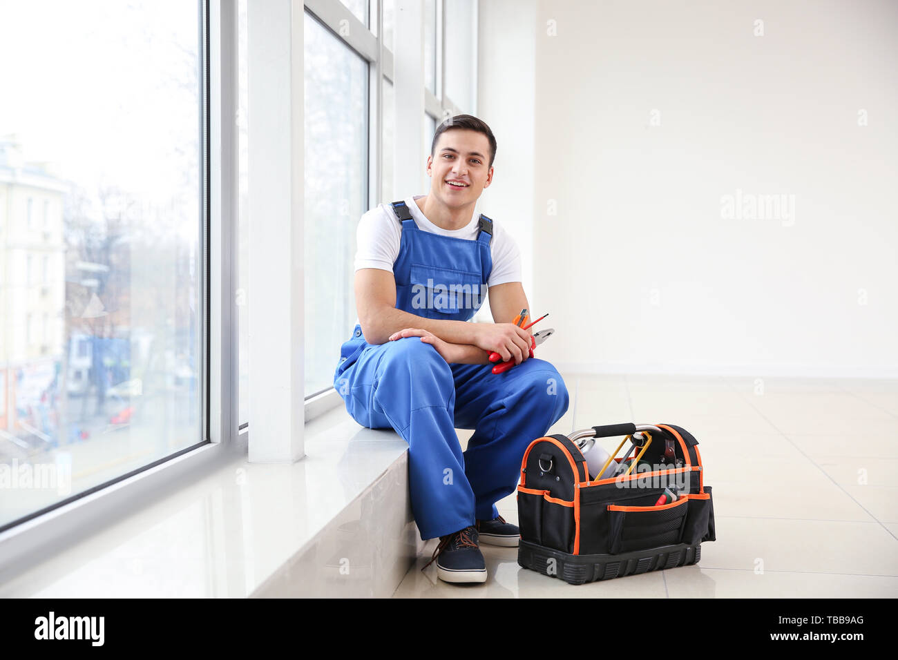 Young worker sitting on window sill in flat Stock Photo