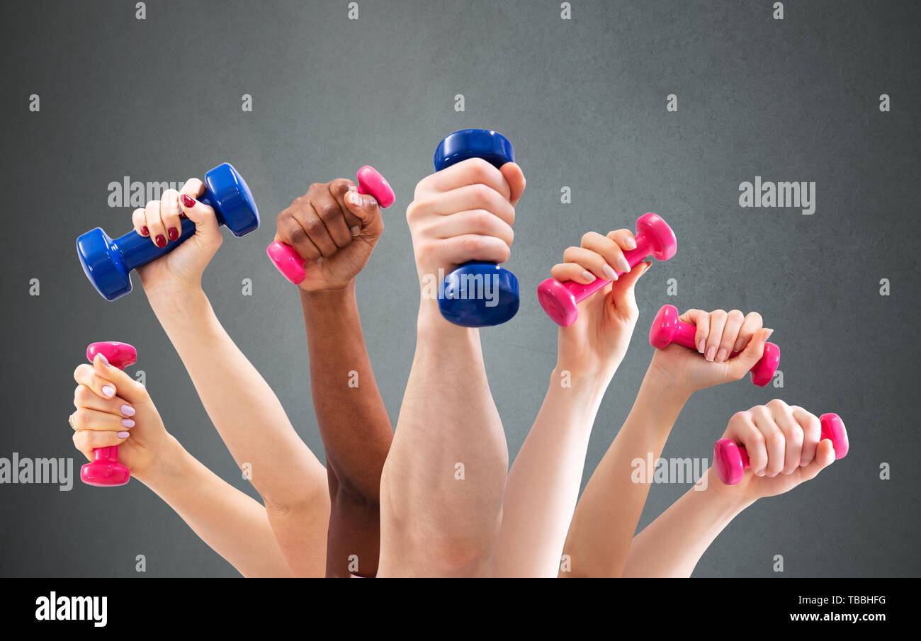 Group Of Man And Woman's Hand Holding Dumbbells In A Row Against Green Background Stock Photo