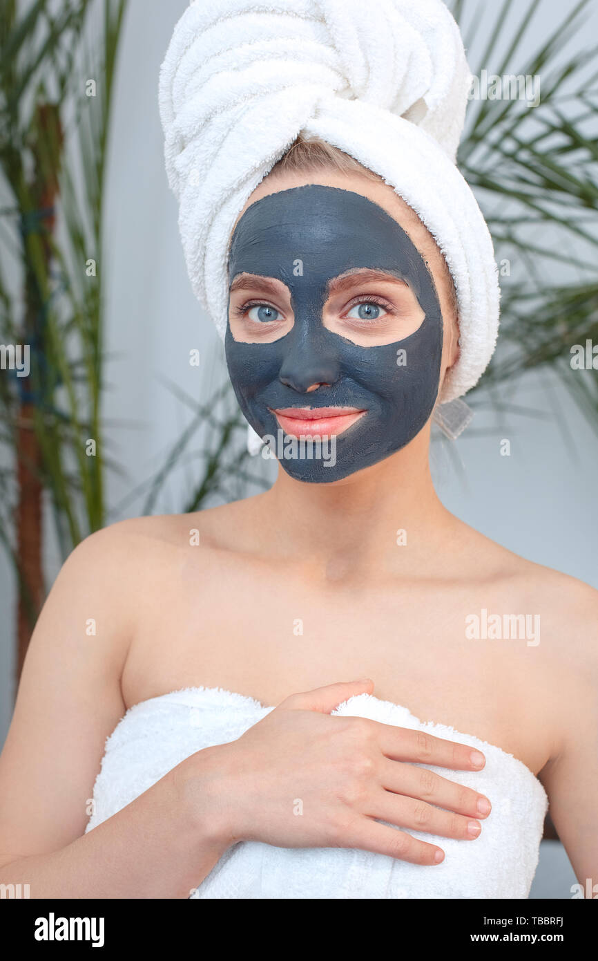 Young woman wearing towel rest at home beauty care standing with a black clay mask on face looking camera smiling happy Stock Photo