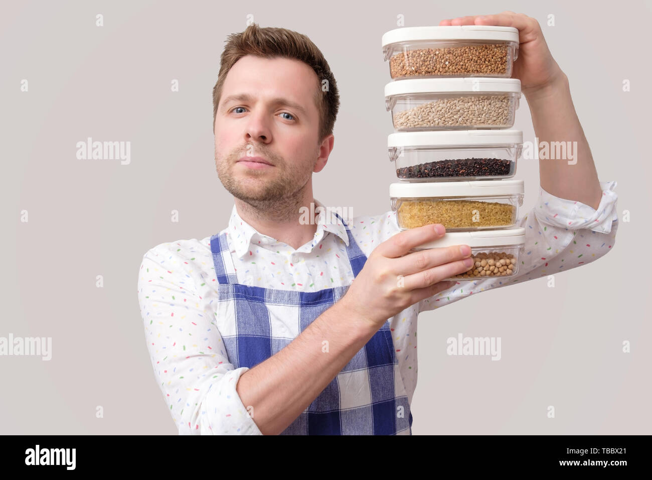 Young smiling man in apron hold several boxes with grains. Stock Photo