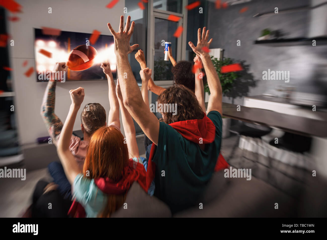 Group of friends watch a football game together on television and rejoice Stock Photo