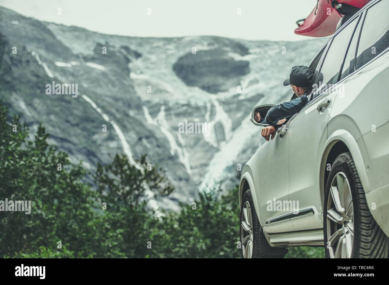 Caucasian Men on a Scenic Mountain Road Trip in the Full Size SUV with Kayak on a Roof. Summer Destinations. Stock Photo