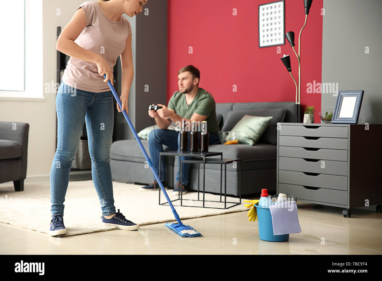 Wife cleaning floor while her lazy husband resting on couch at home ...