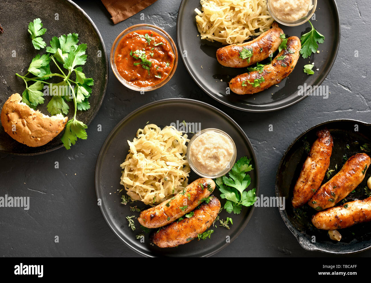Grilled sausages with stewed sauerkraut and horseradish on plate over black stone background. Top view, flat lay Stock Photo