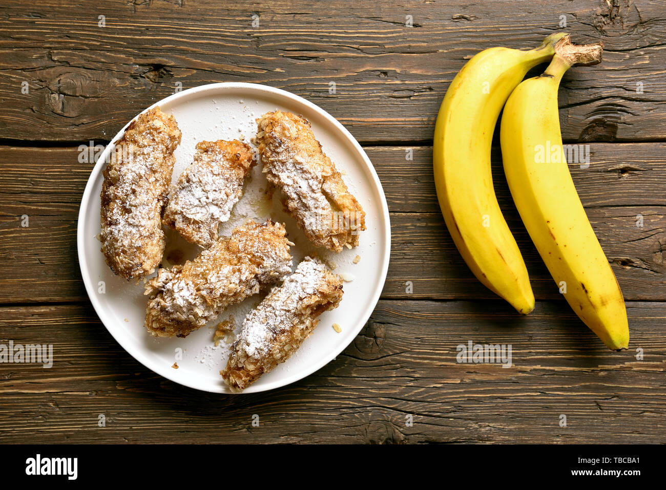 Tasty deep fried bananas on plate over wooden background. Dessert from