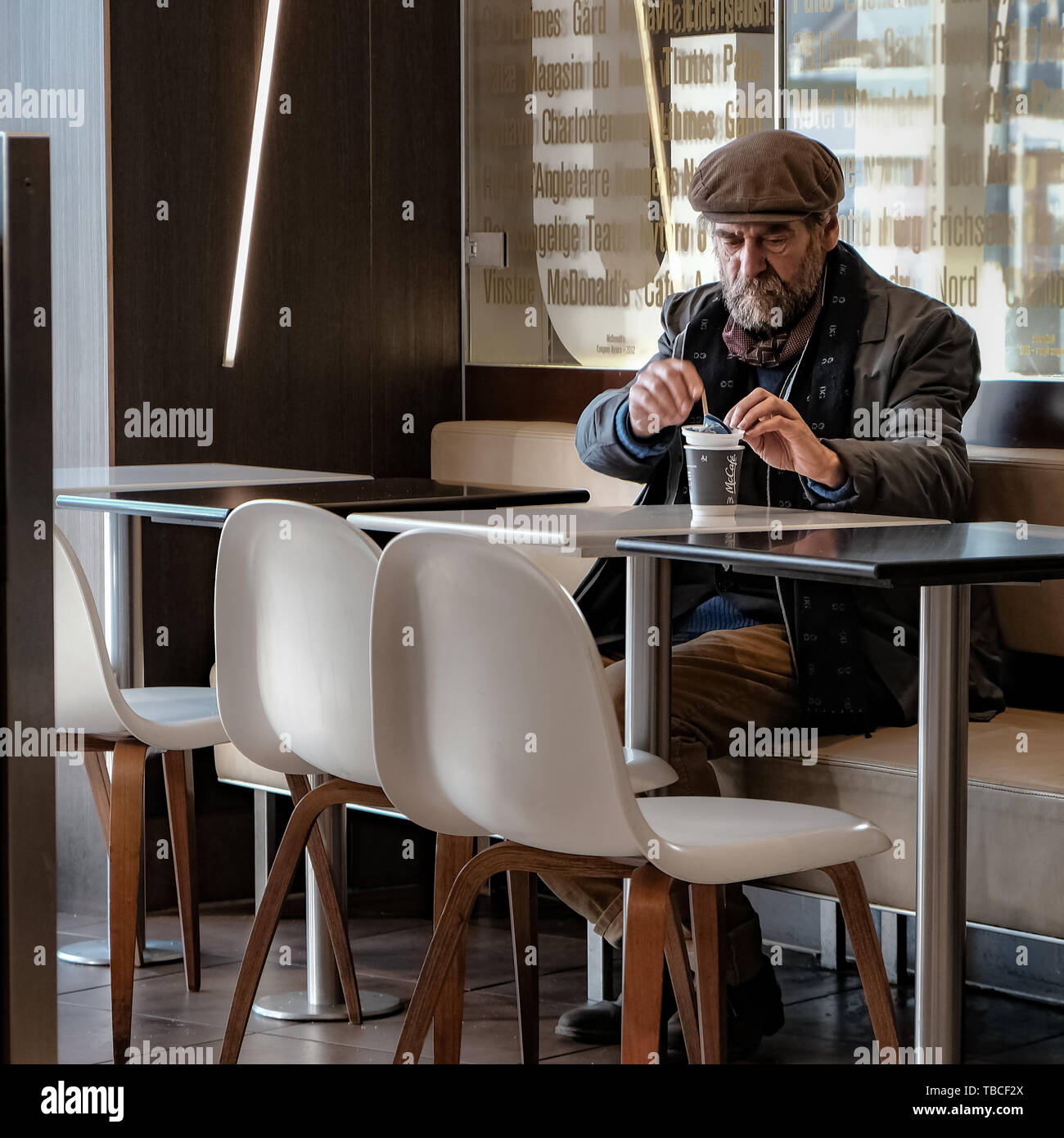 A Scandinavian man wearing a hat is having a drink at a local fast food place, Copenhagen
