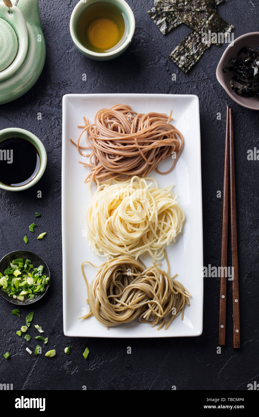 Assortment of Japanese soba noodles with sauce and garnishes. Black slate background. Top view