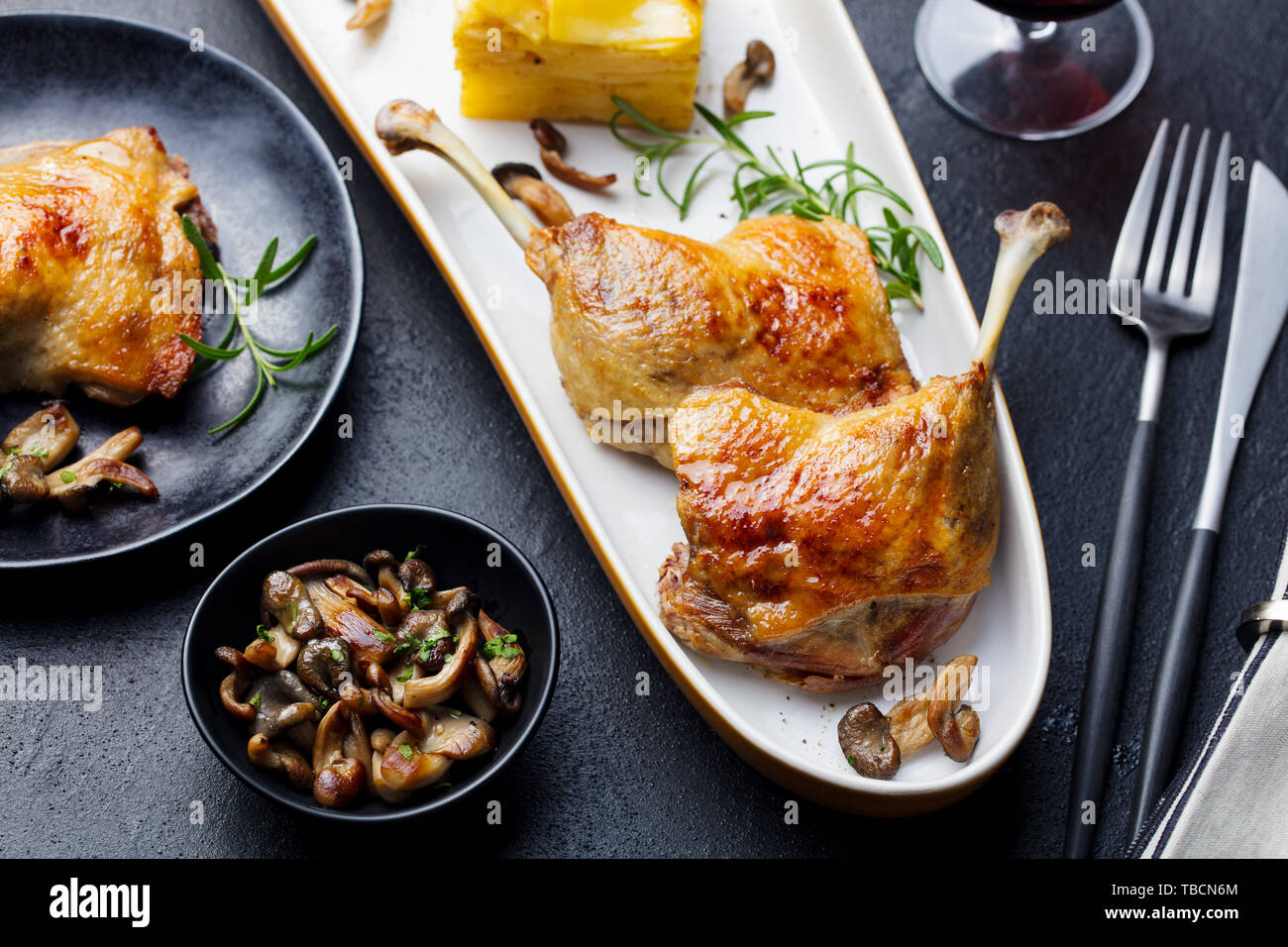 Duck legs confit with potato gratin and mushroom on a plate. Close up. Stock Photo