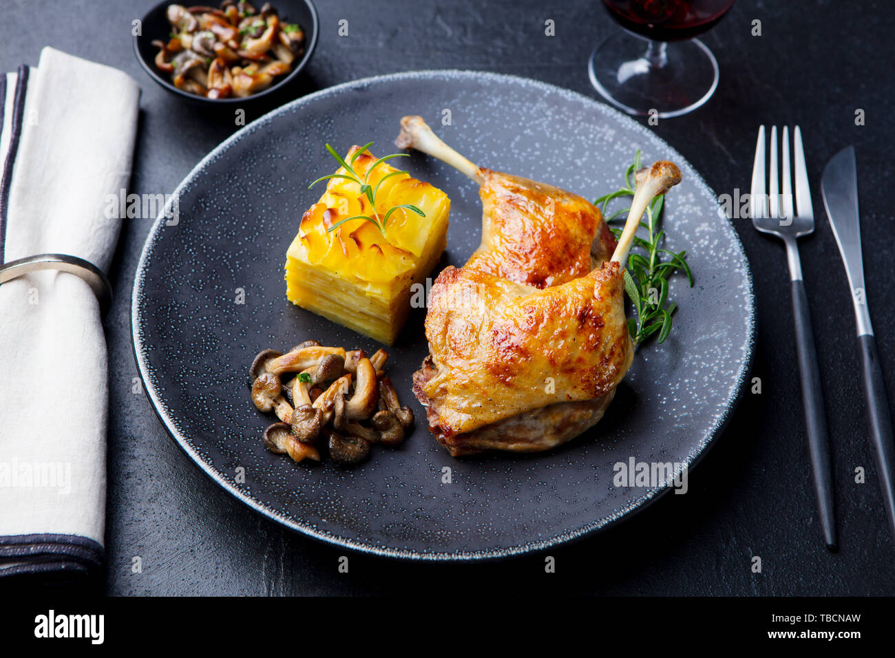 Duck legs confit with potato gratin and mushroom on a plate. Slate background. Stock Photo