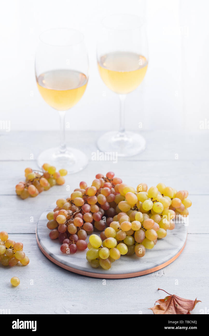 Fresh grape on marble cutting board with glasses of white wine. Wooden background. Stock Photo