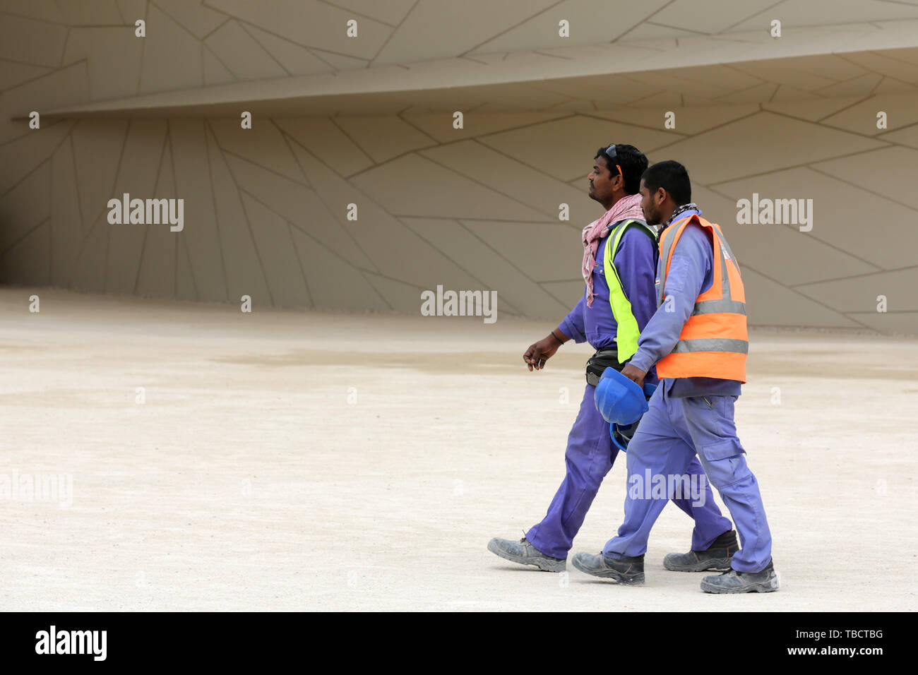 Doha, Qatar 11 April, 2019 Two workers in uniforms with helmets walk