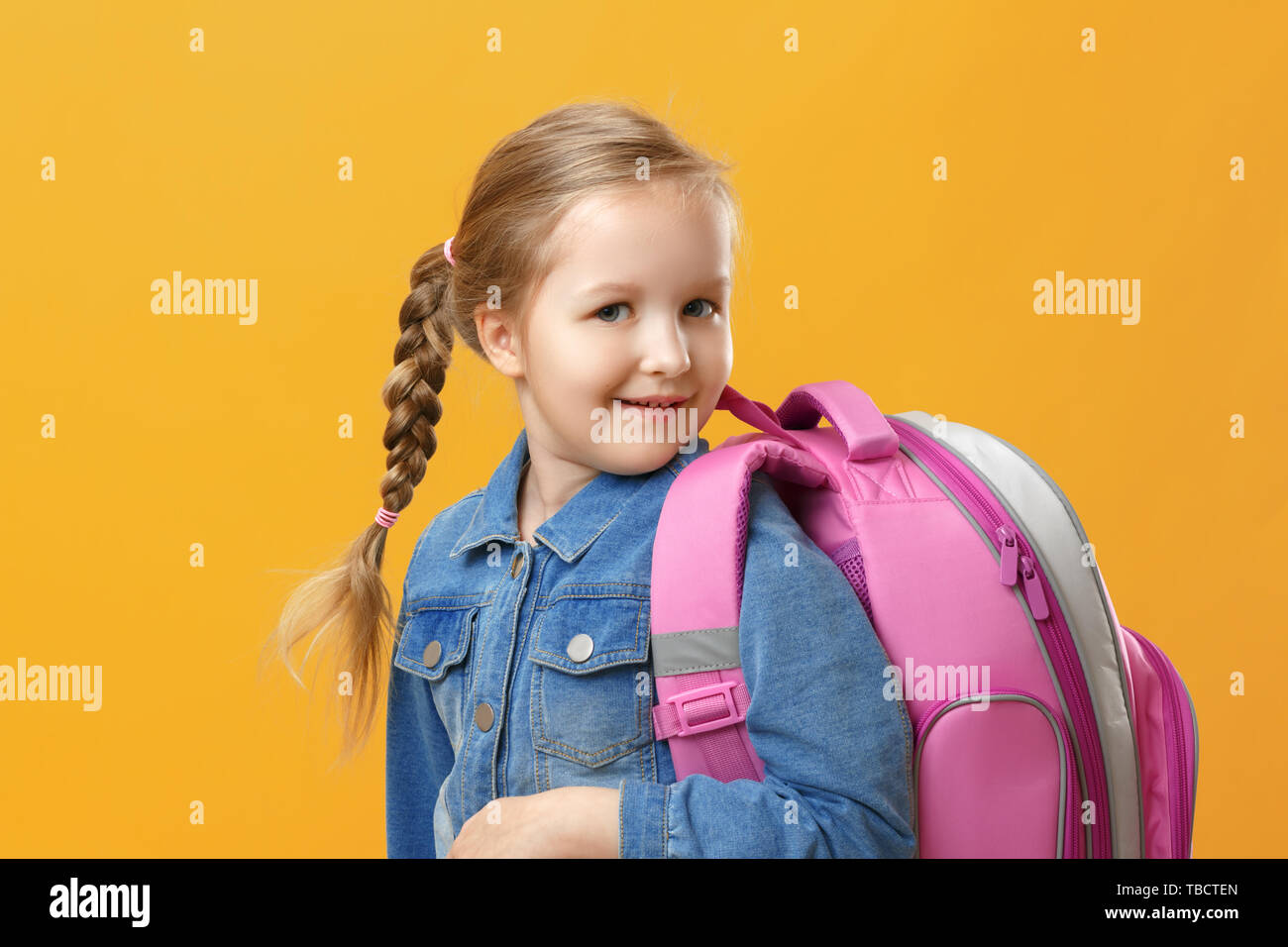 Portrait of a little girl schoolgirl with a backpack on a yellow background. Back to school. The concept of education. Stock Photo