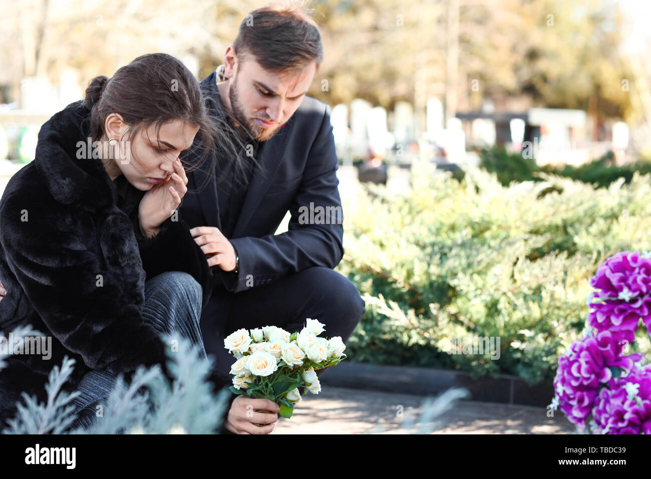 Couple putting flowers on grave of their relative at funeral Stock