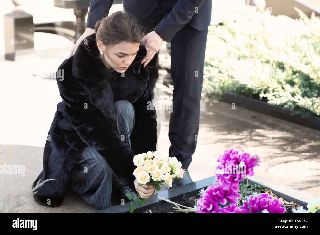 Couple putting flowers on grave of their relative at funeral Stock