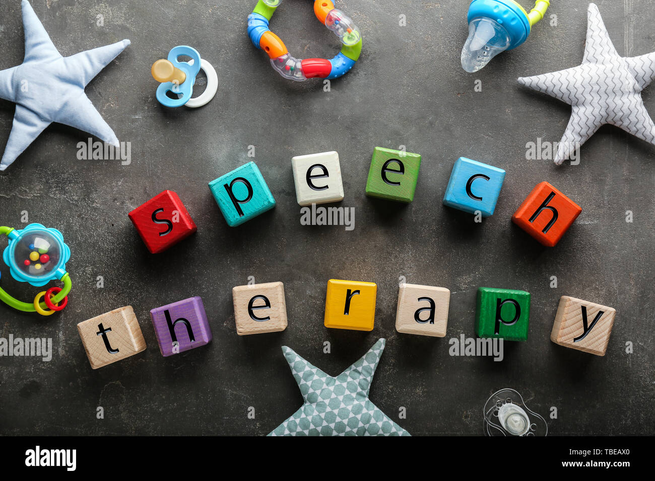 Cubes with text SPEECH THERAPY, pacifiers and toys on grey background