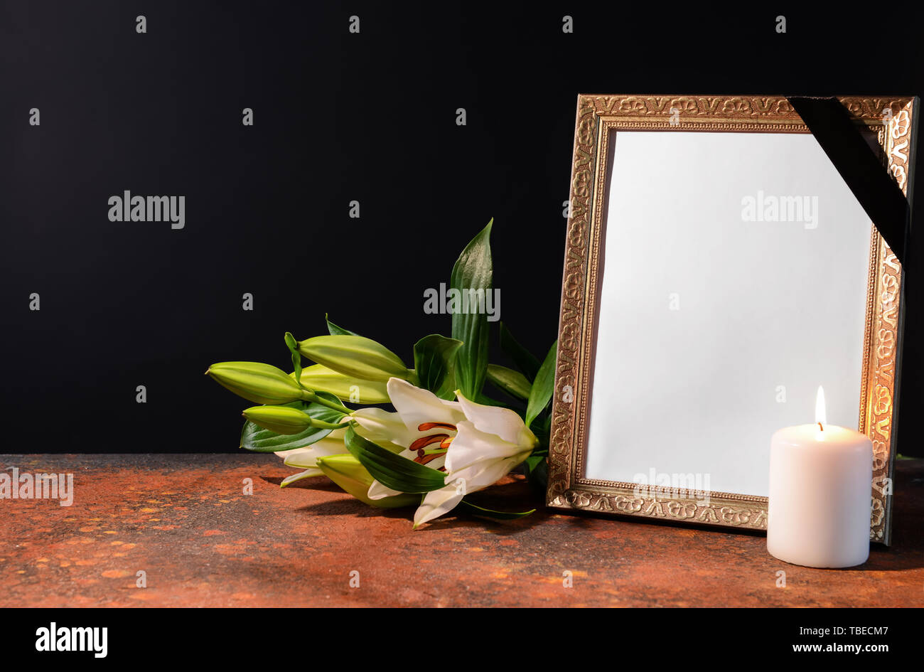 Blank funeral frame, candle and flowers on table against black