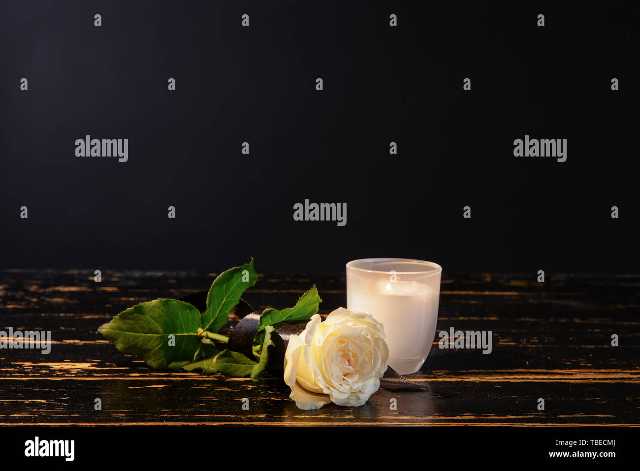 Burning candle and flower on table against black background Stock Photo