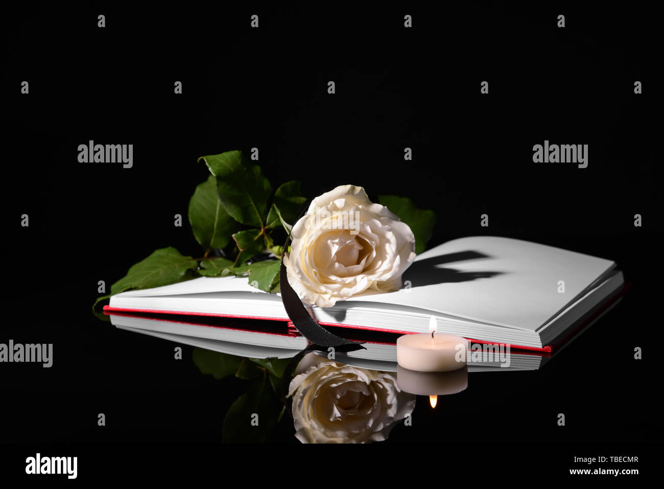 Open book, flower, black ribbon and burning candle on dark background