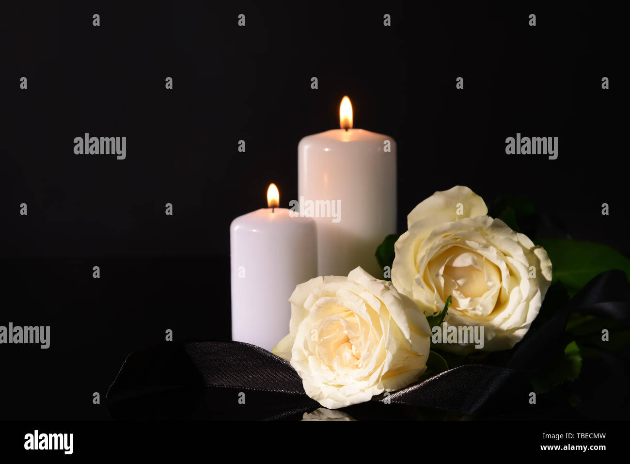 Burning candles, mourning ribbon and flowers on black background Stock