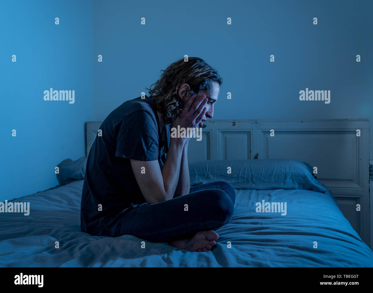 Devastated millennial man crying sad feeling hurt and hopeless suffering Depression. Depressed teenager victim of bullying or abuse sitting on bed alo Stock Photo