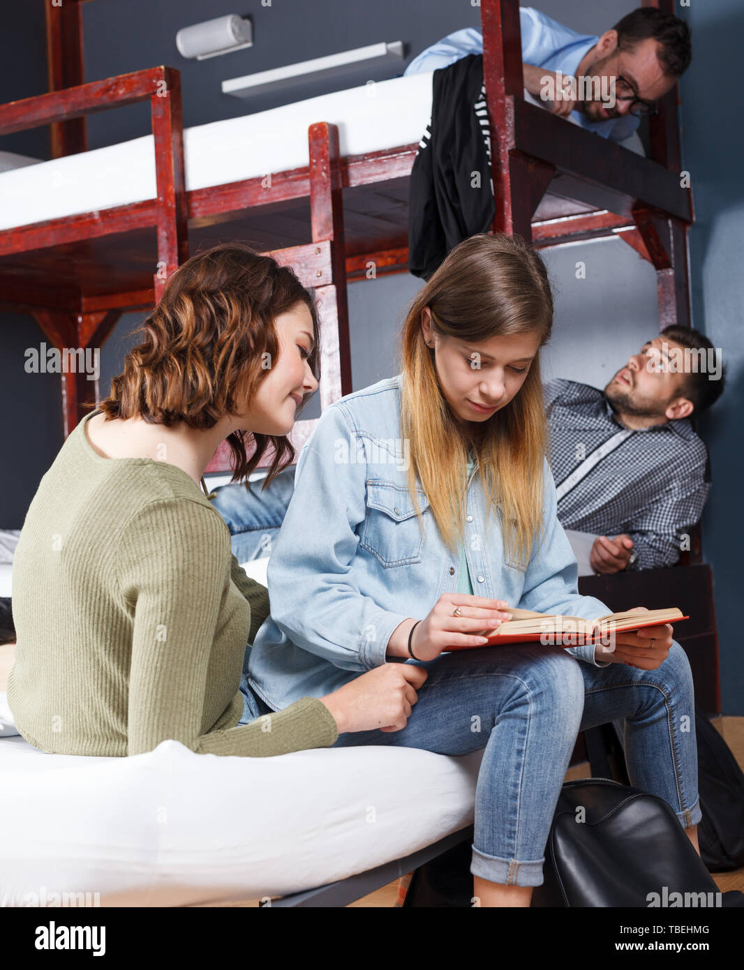 Portrait of two attractive girls reading book while resting in bedroom of modern hostel Stock Photo