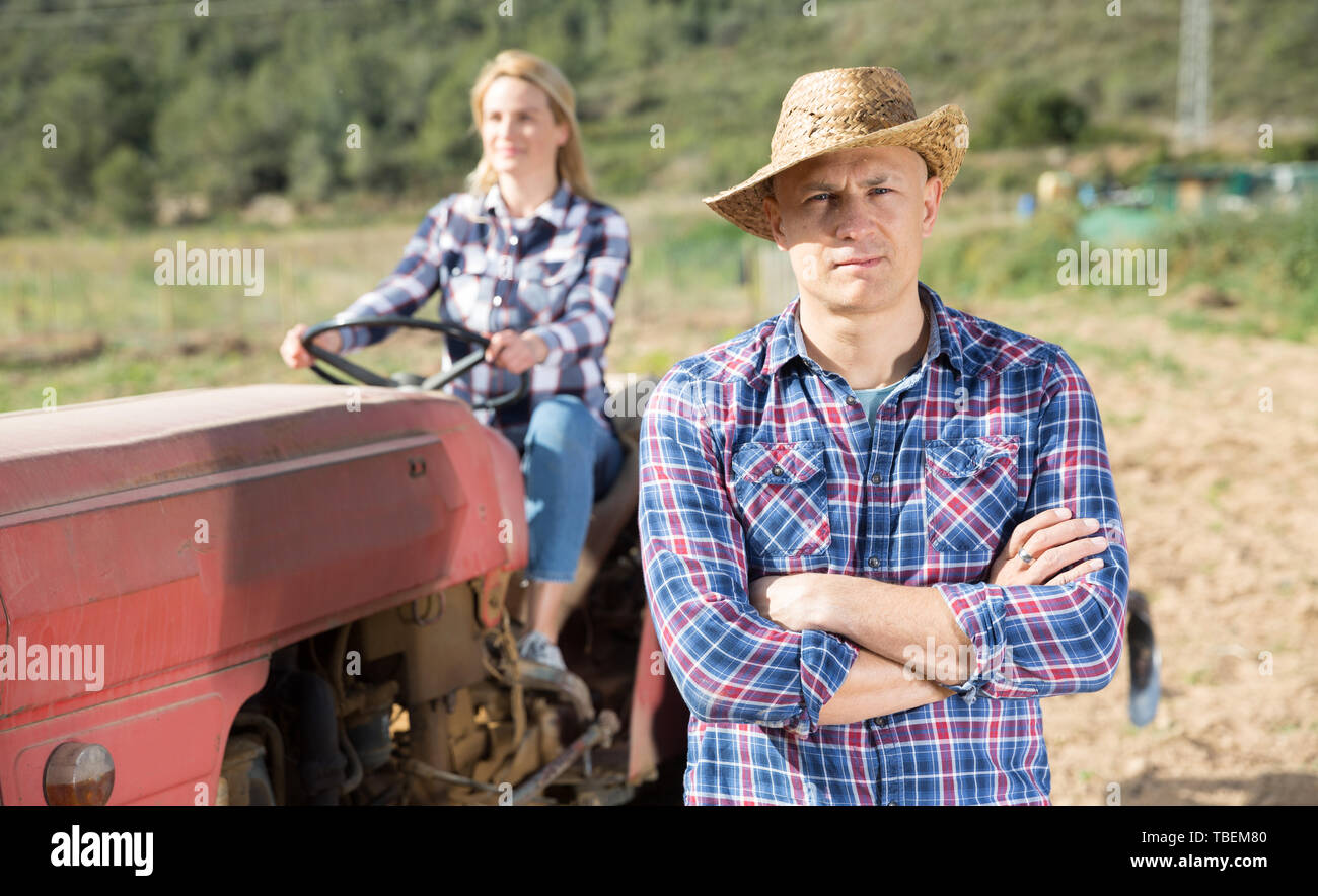 Portrait of male farmer on background with his wife tilling soil on ...