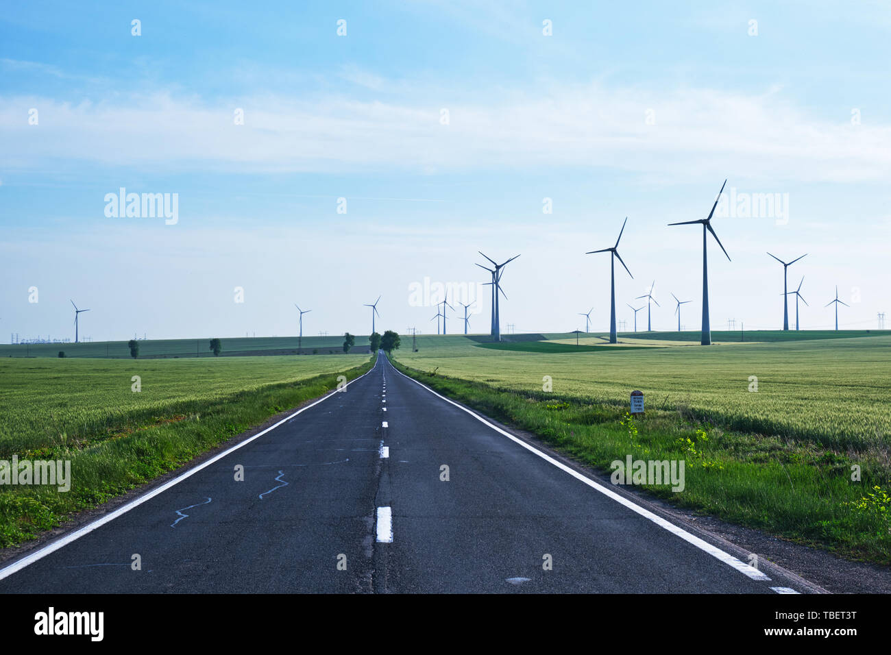 Road going forward with wind turbines on its sides and into the distance, on blue skies. Concept for new, better, non polluting, sustainable energy so Stock Photo