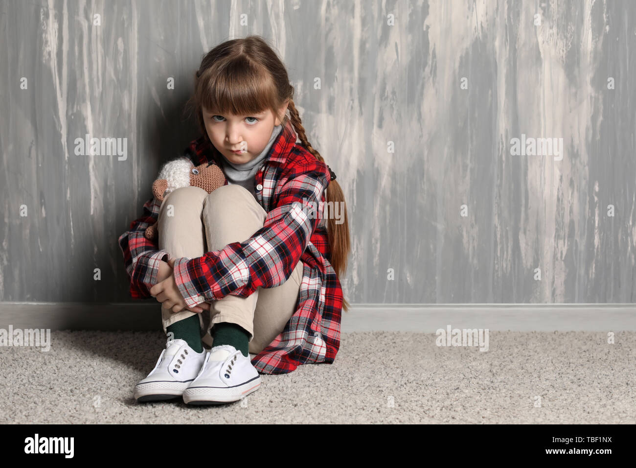 Sad little girl sitting on floor near grey wall Stock Photo - Alamy