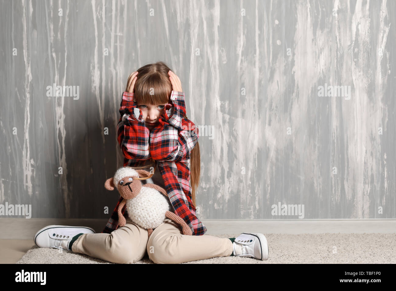 Sad little girl sitting on floor near grey wall Stock Photo - Alamy