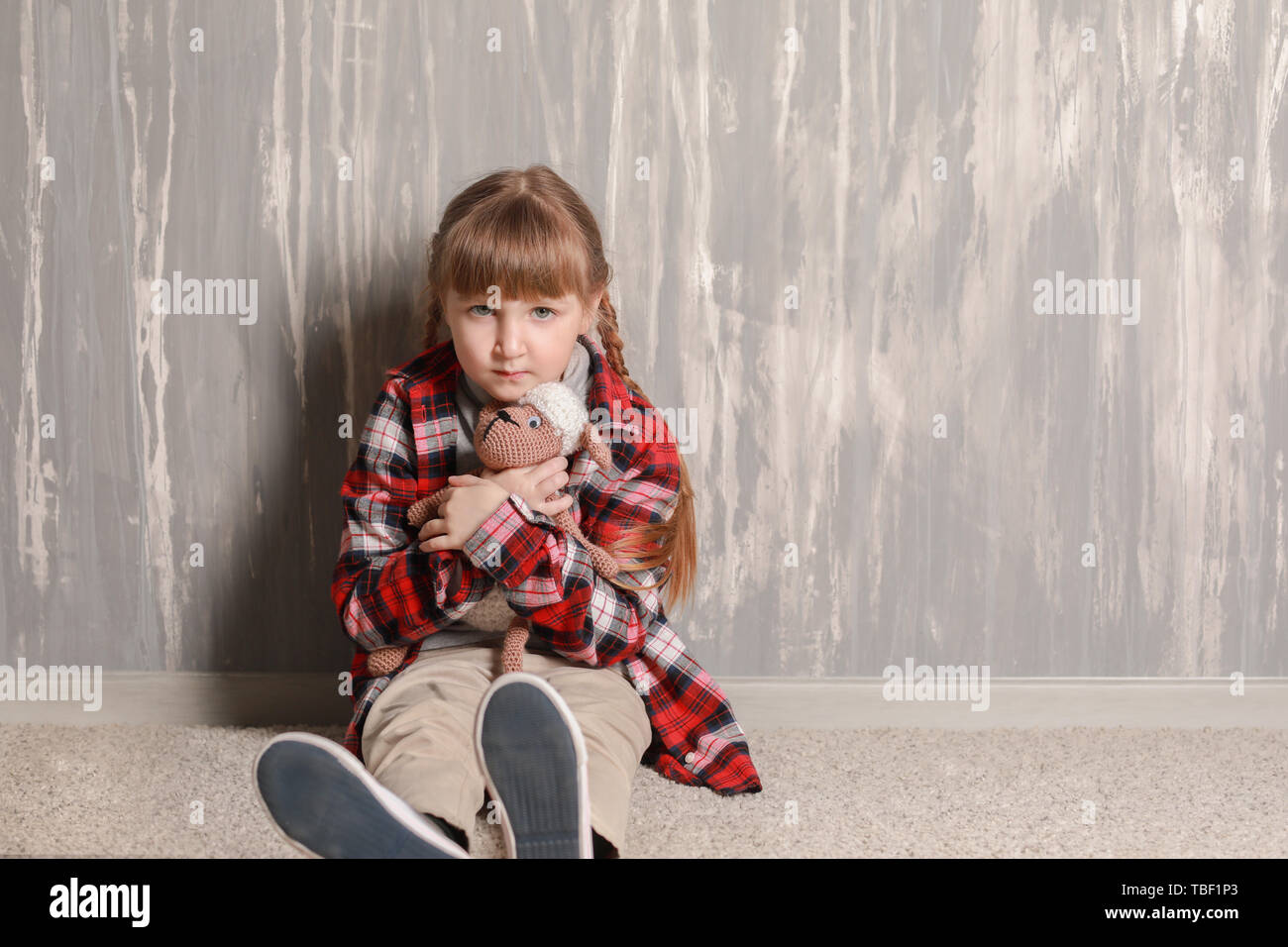 Sad little girl sitting on floor near grey wall Stock Photo - Alamy