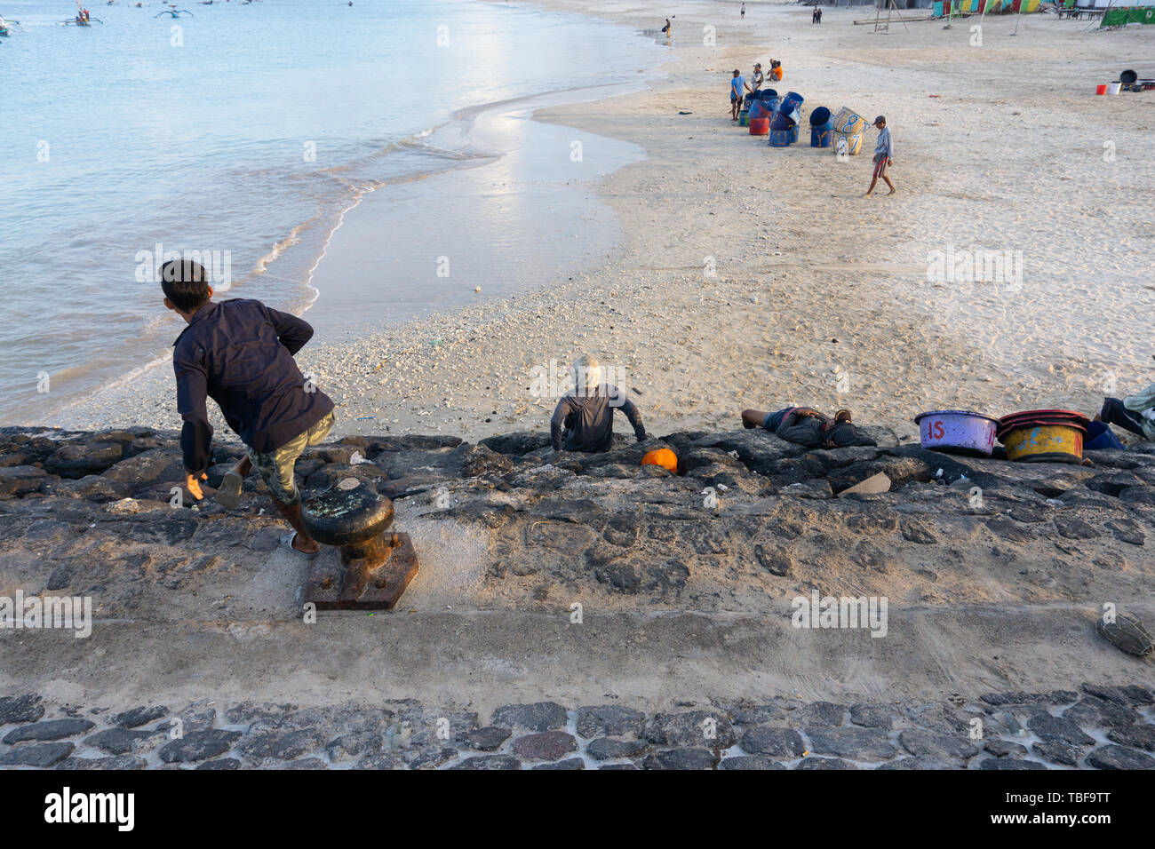 BALI/INDONESIA-MAY 15 2019: Some fishermen carrying fish are resting on the edge of the harbor. They were waiting for the fishing boat tied to the sea Stock Photo