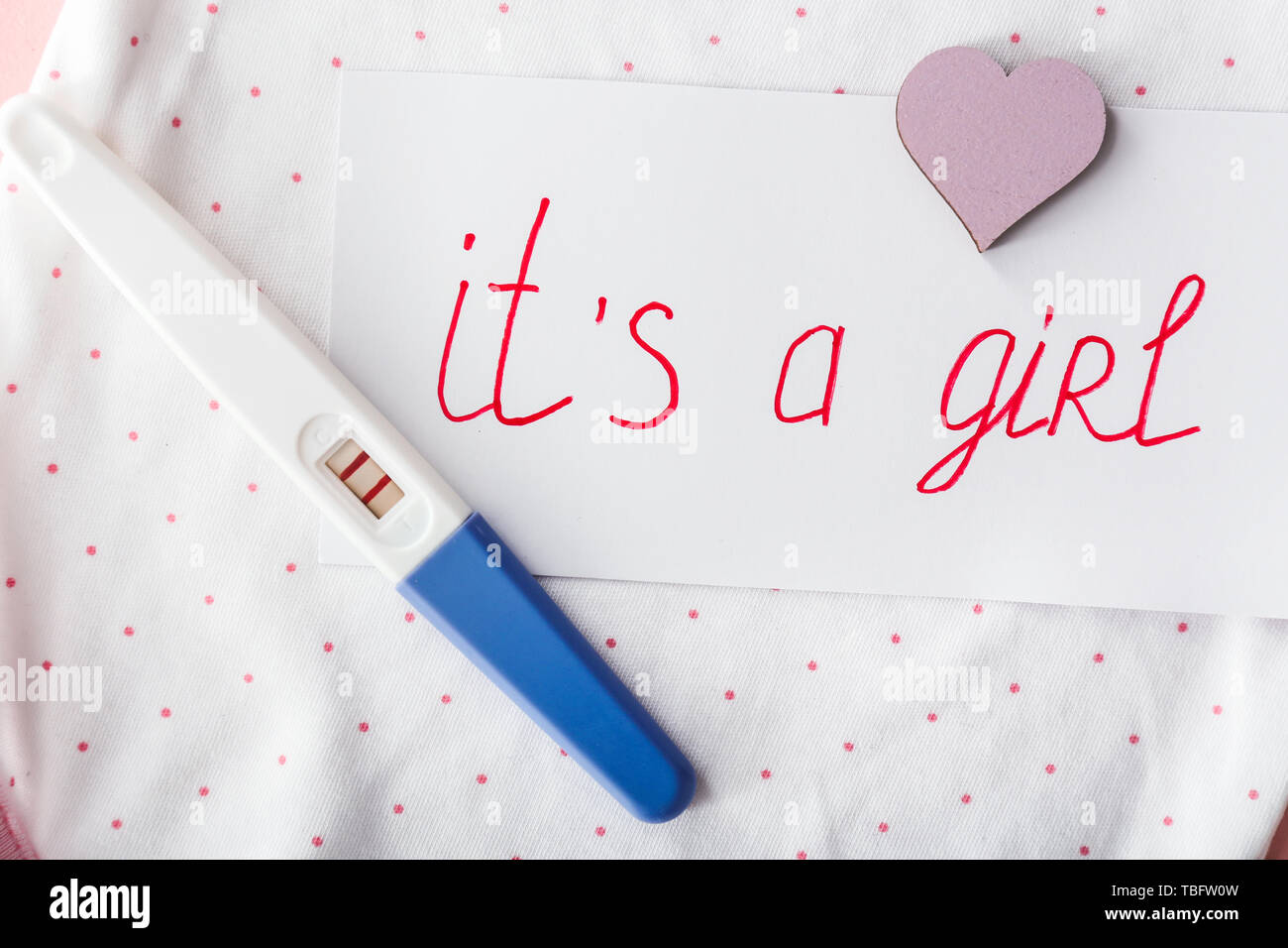 Paper with text IT'S A GIRL and pregnancy test on baby clothes ... Paper with text IT'S A GIRL and pregnancy test on baby clothes ...