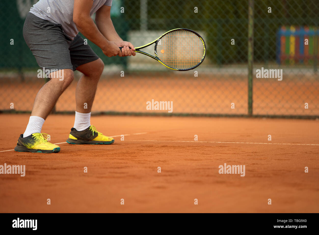 Close up of man holding tennis racket on clay court. On court is sunset