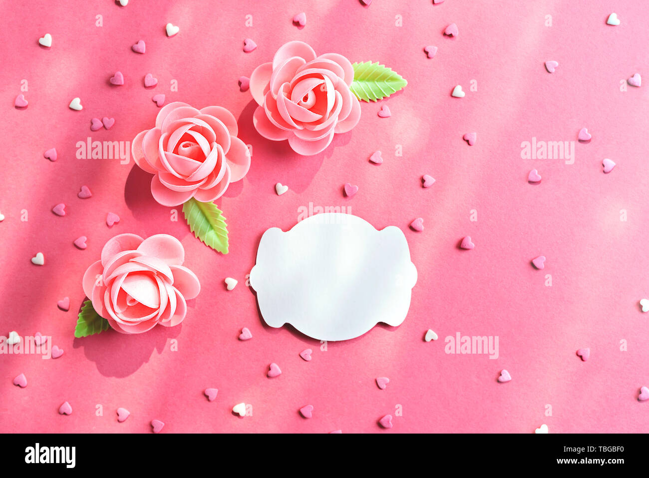 Pink background with sweet flowers and heart shaped confetti pastry. With space for a note. Flat lay Stock Photo
