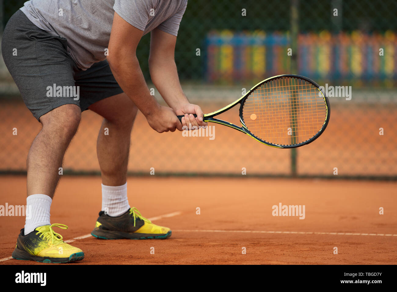 Close up of man holding tennis racket on clay court. On court is sunset