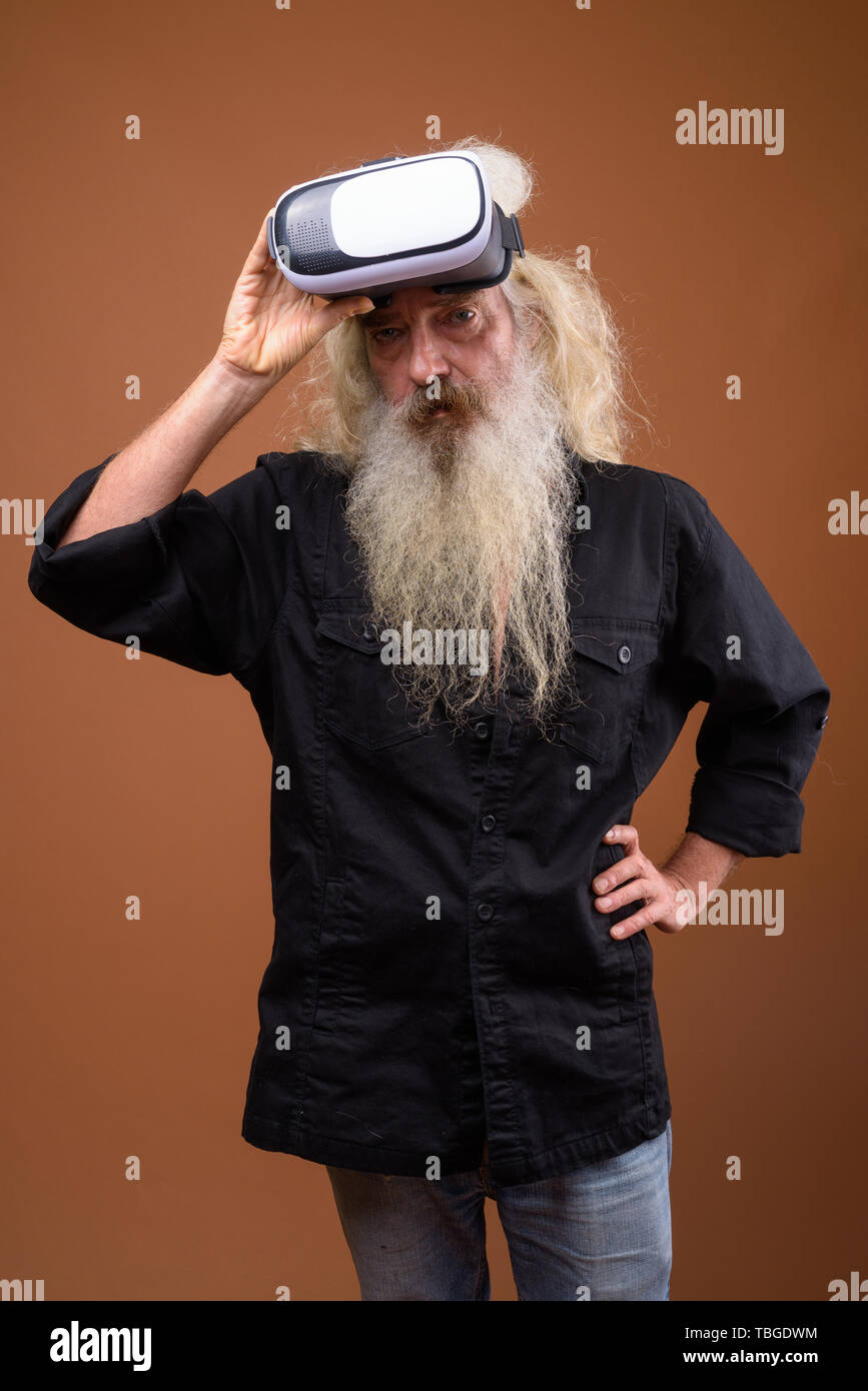 Studio shot of senior bearded man wearing black shirt against brown background Stock Photo