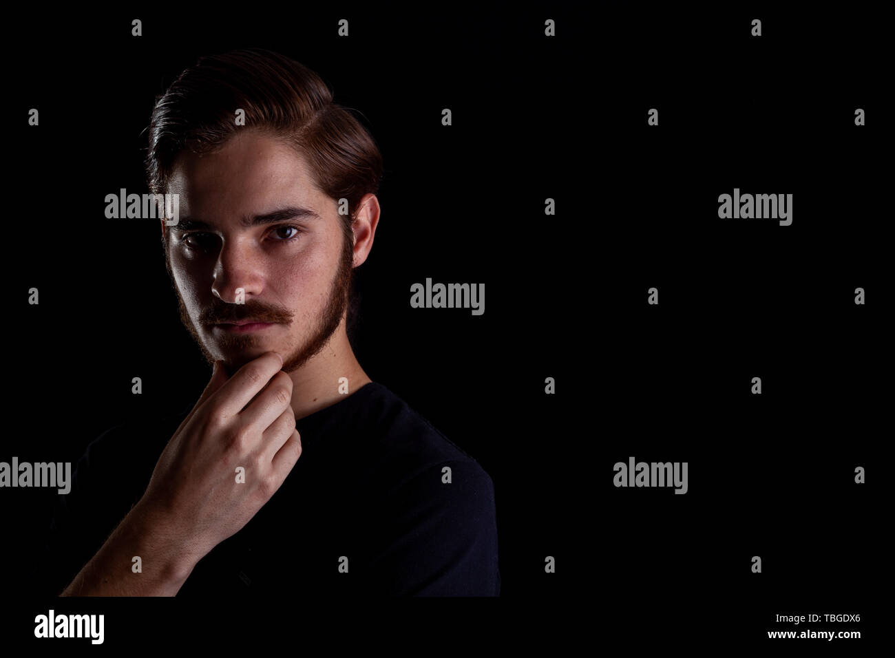 Young adult male looking sinister or contemplative. Color expressive dark and moody series. Concept image for corporate scheming. Hand under chin. Stock Photo