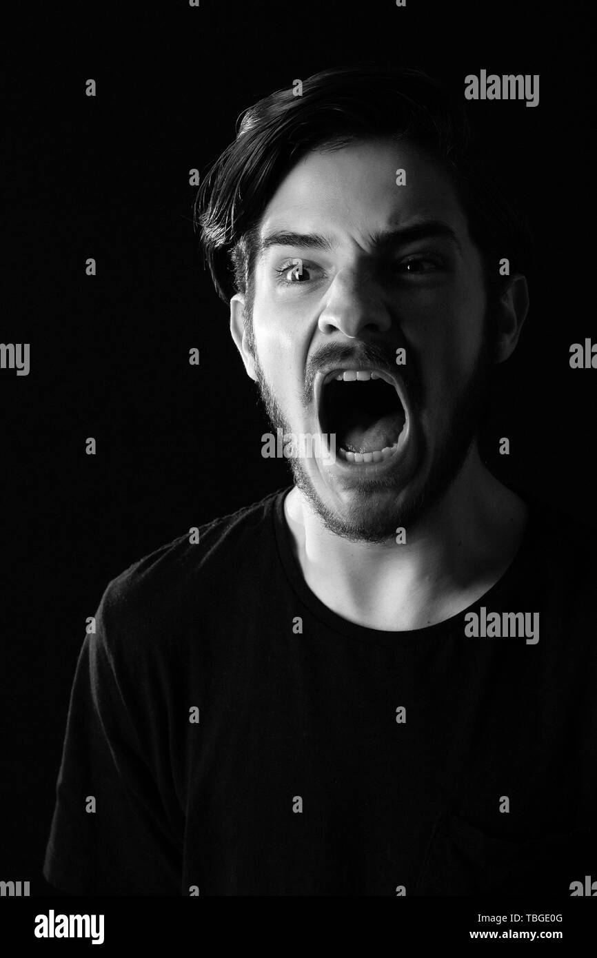 Close up of young adult male looking left screaming. Monotone, black and white for dramatic effect, dark and moody series. Concept image for terror, d Stock Photo