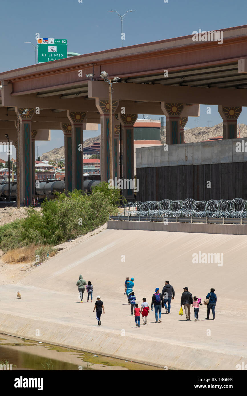 A group of migrants, including children, walk along the banks of the Rio Grande towards a gap in the Border Wall under a new highway overpass near dow Stock Photo