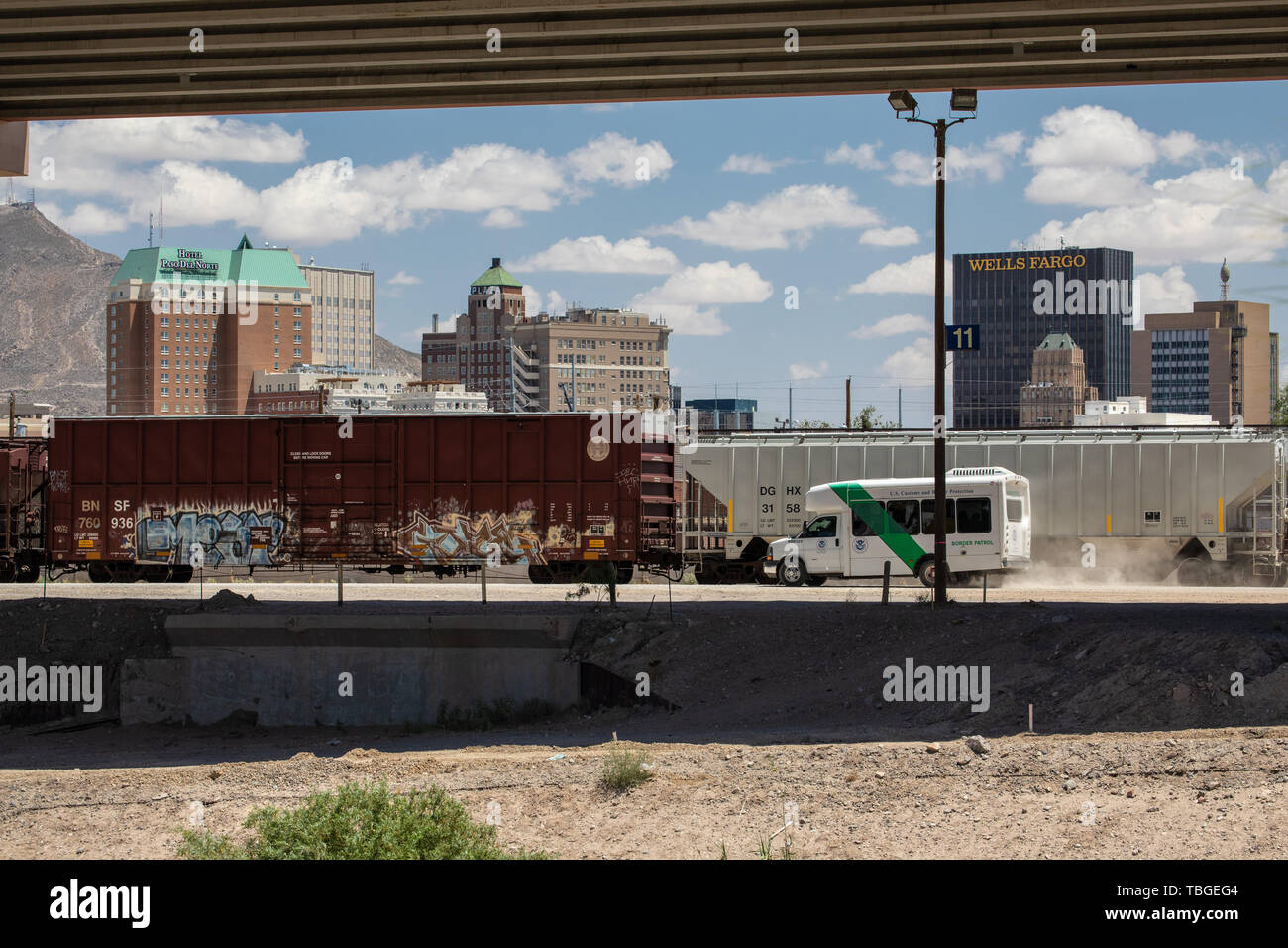 A Border Patrol transport van  drives along the US Mexico border to pick up a group of migrants, with the downtown El Paso skyline in the background,  Stock Photo