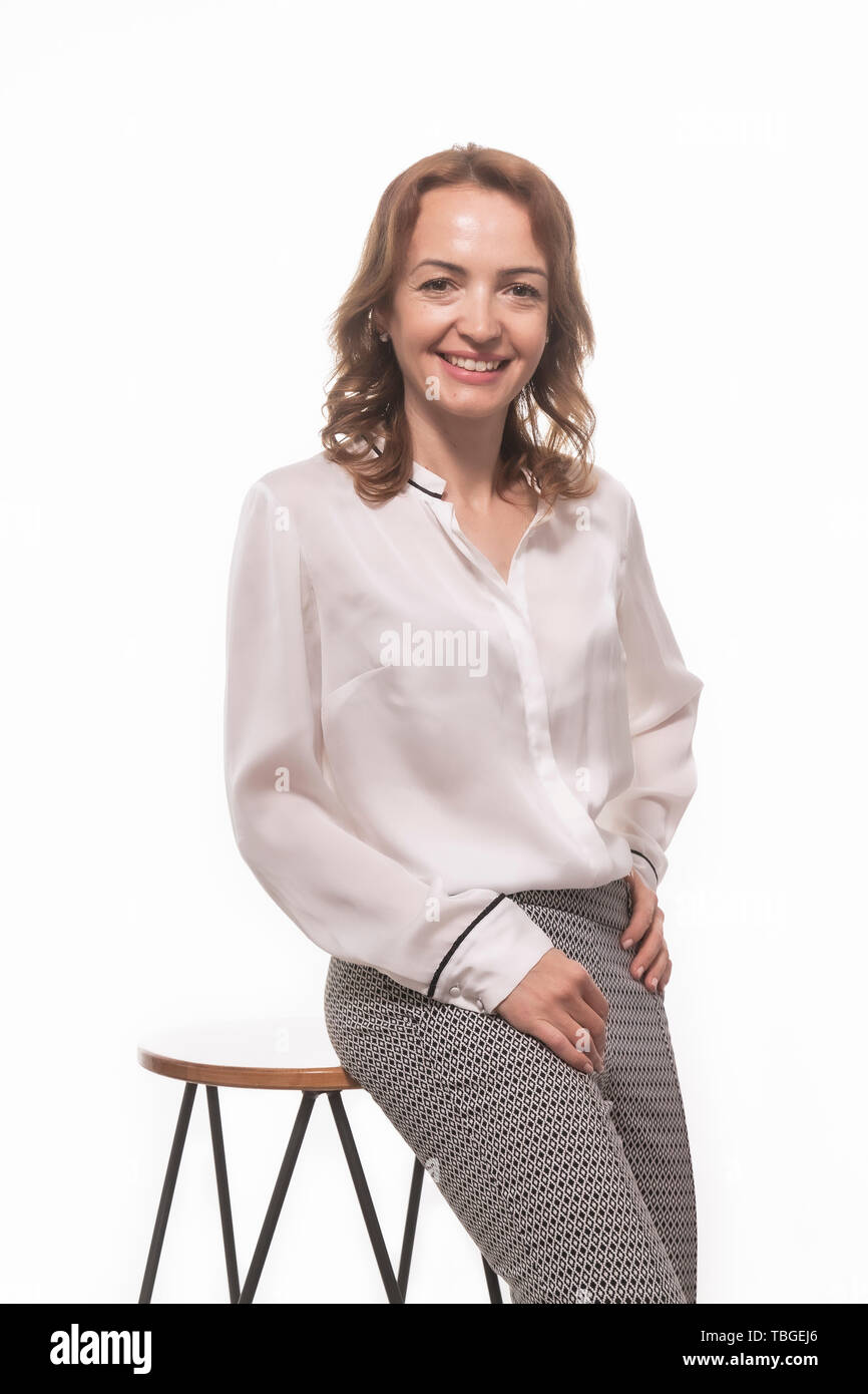 One mature woman, 40 years old, businesswoman portrait posing, leaning on a bar stool. White background behind. Stock Photo